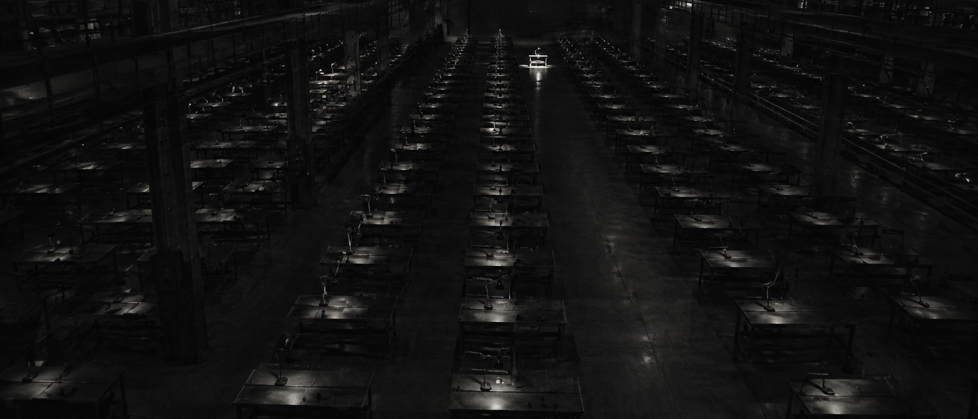 A vast dark hall of identical desks, one workstation lit in the distance